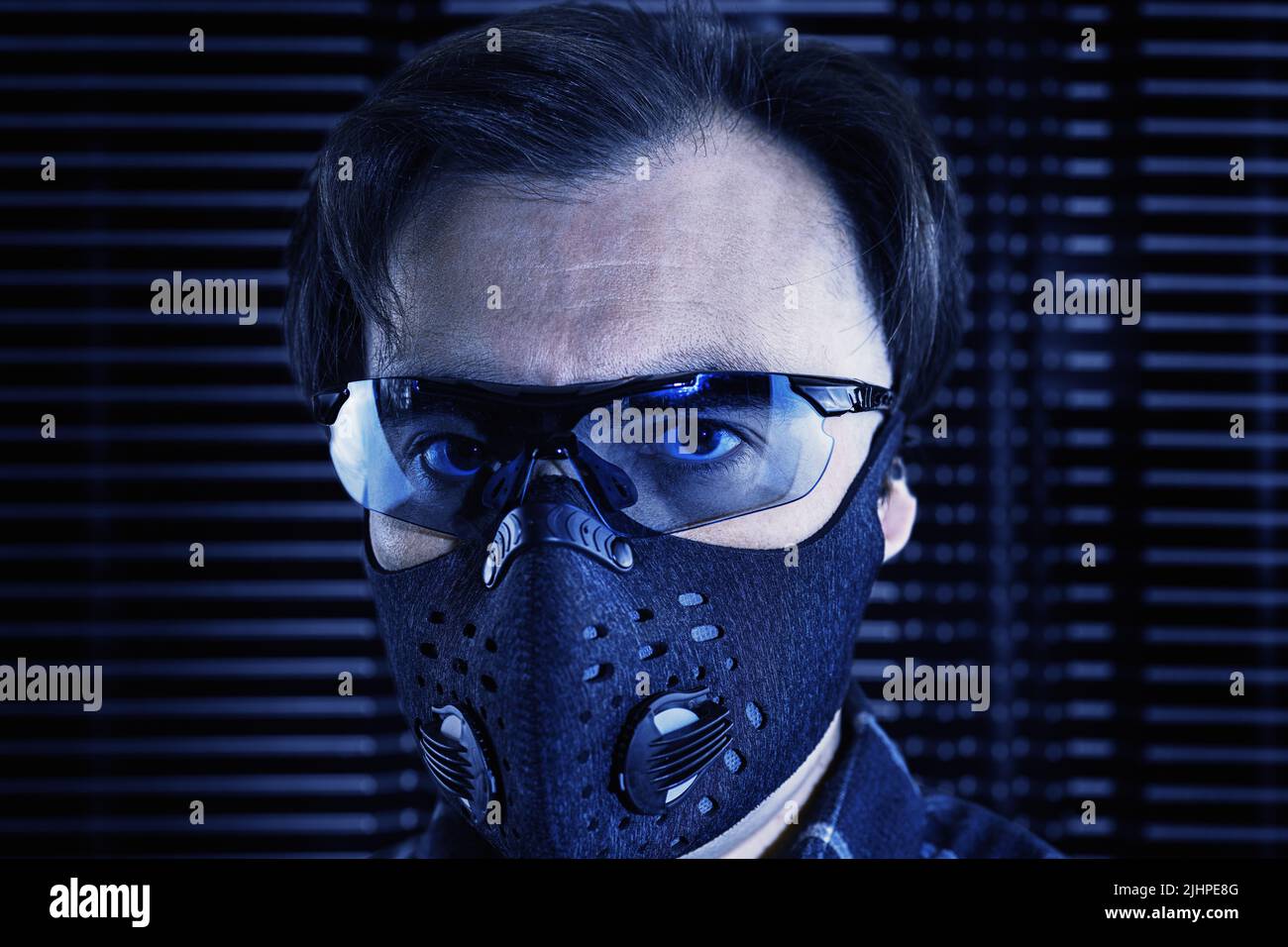 A mid age man in sunglasses and a respiratory mask on a futuristic metal background. Futuristic portrait in industrial technogenic style Stock Photo