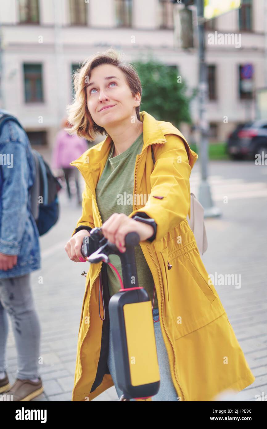 Girl in a yellow raincoat with a yellow electric scooter on a city street. Live toned image Stock Photo