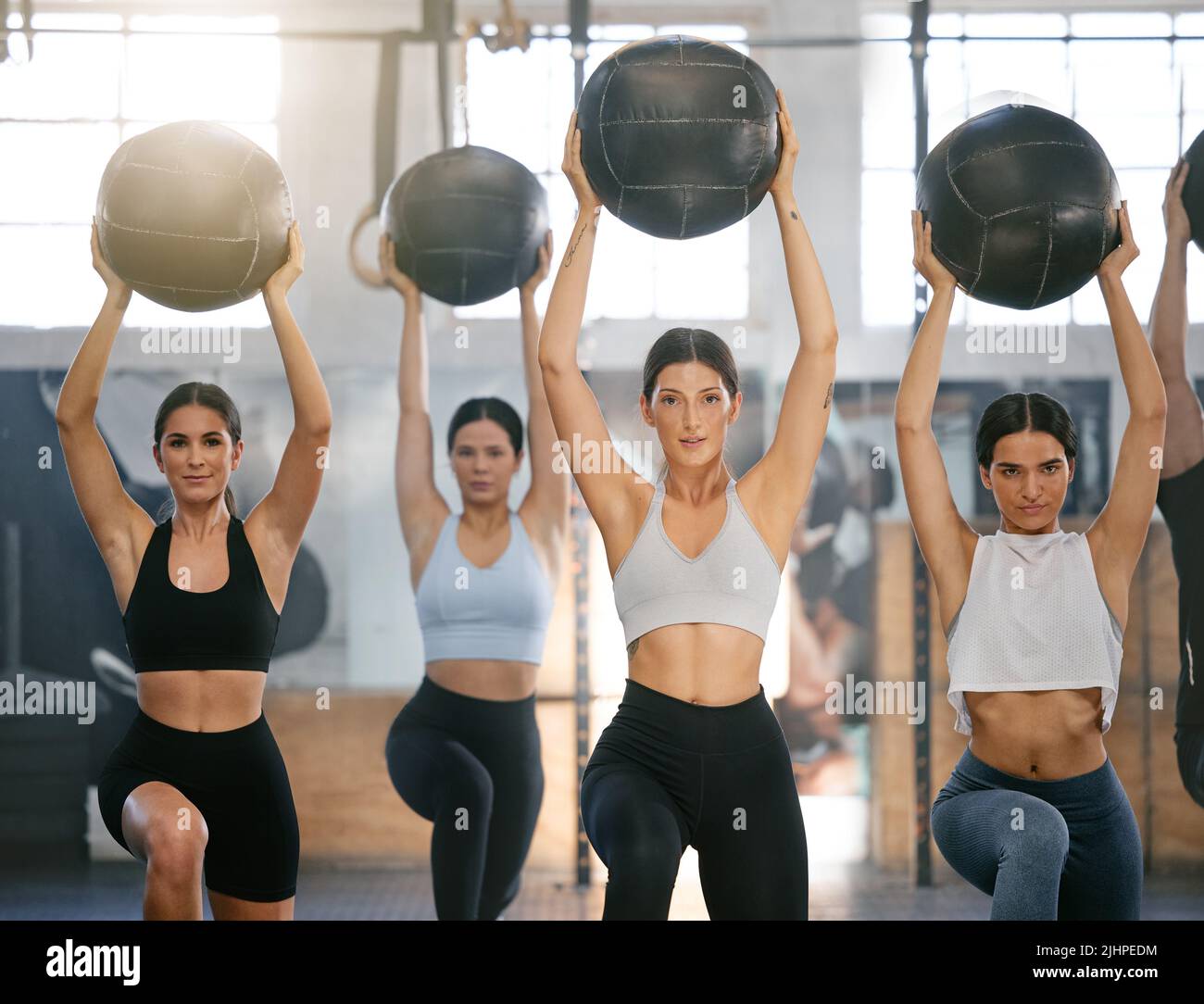 Diverse group of active young people doing overhead medicine ball lunge exercises while training together in a gym. Focused athletes challenging Stock Photo