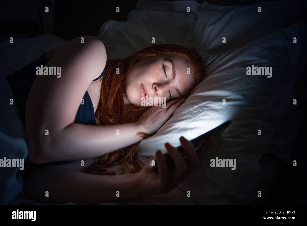 One woman holding mobile phone in bed late at night Stock Photo