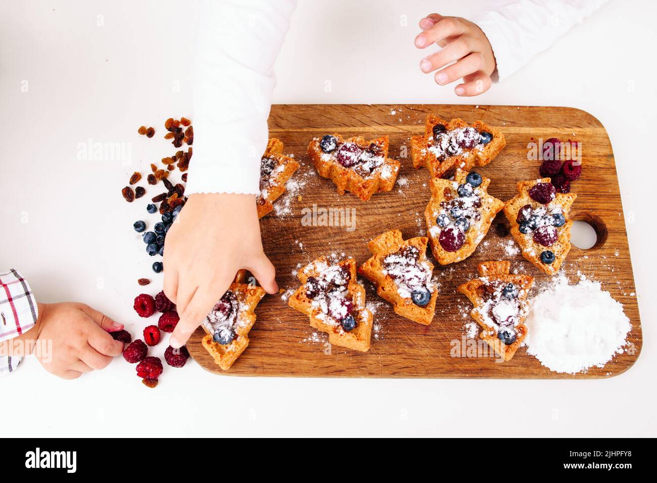 Girl put sweet cakes on board, little boy hand Stock Photo