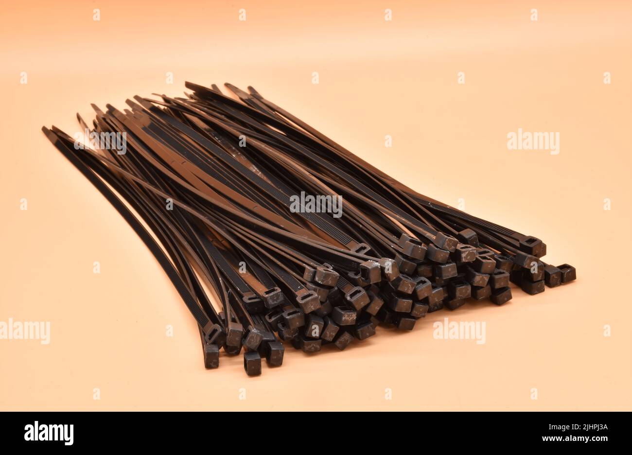 Black cable ties isolated on orange background. Plastic Tie Wraps. Stock Photo