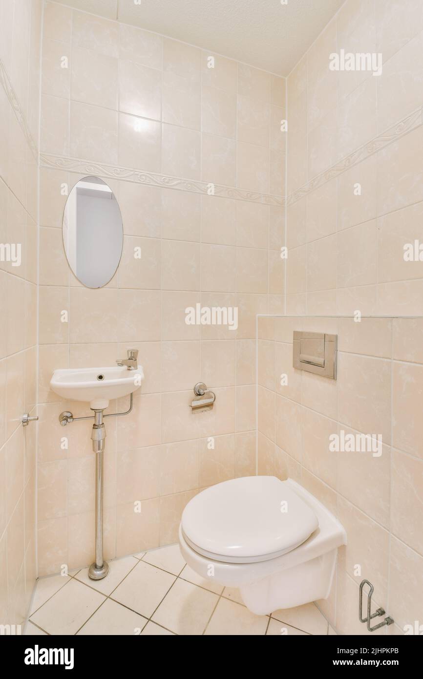 Interior of narrow restroom with sink and wall hung toilet with white