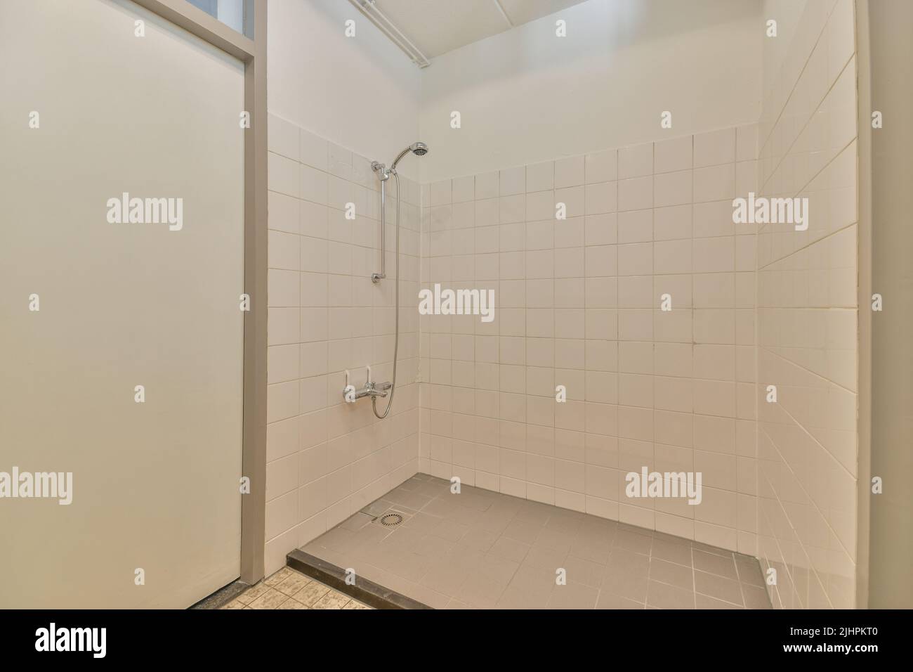 Shower faucets attached to tiled wall near glass partition and ornamental curtail in washroom at