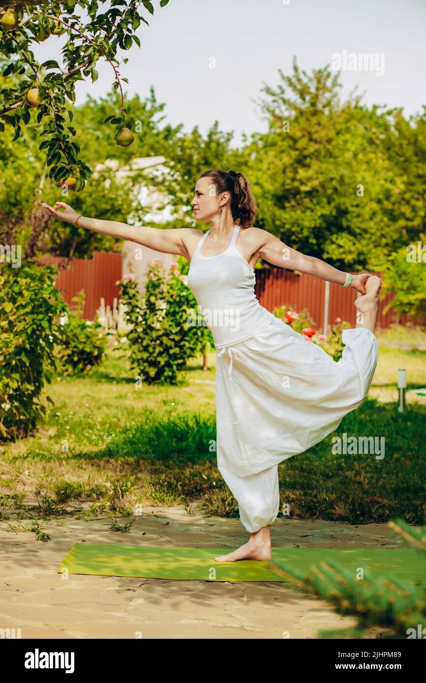 Young woman practices yoga in the summer garden: Natarajasana, Lord of ...