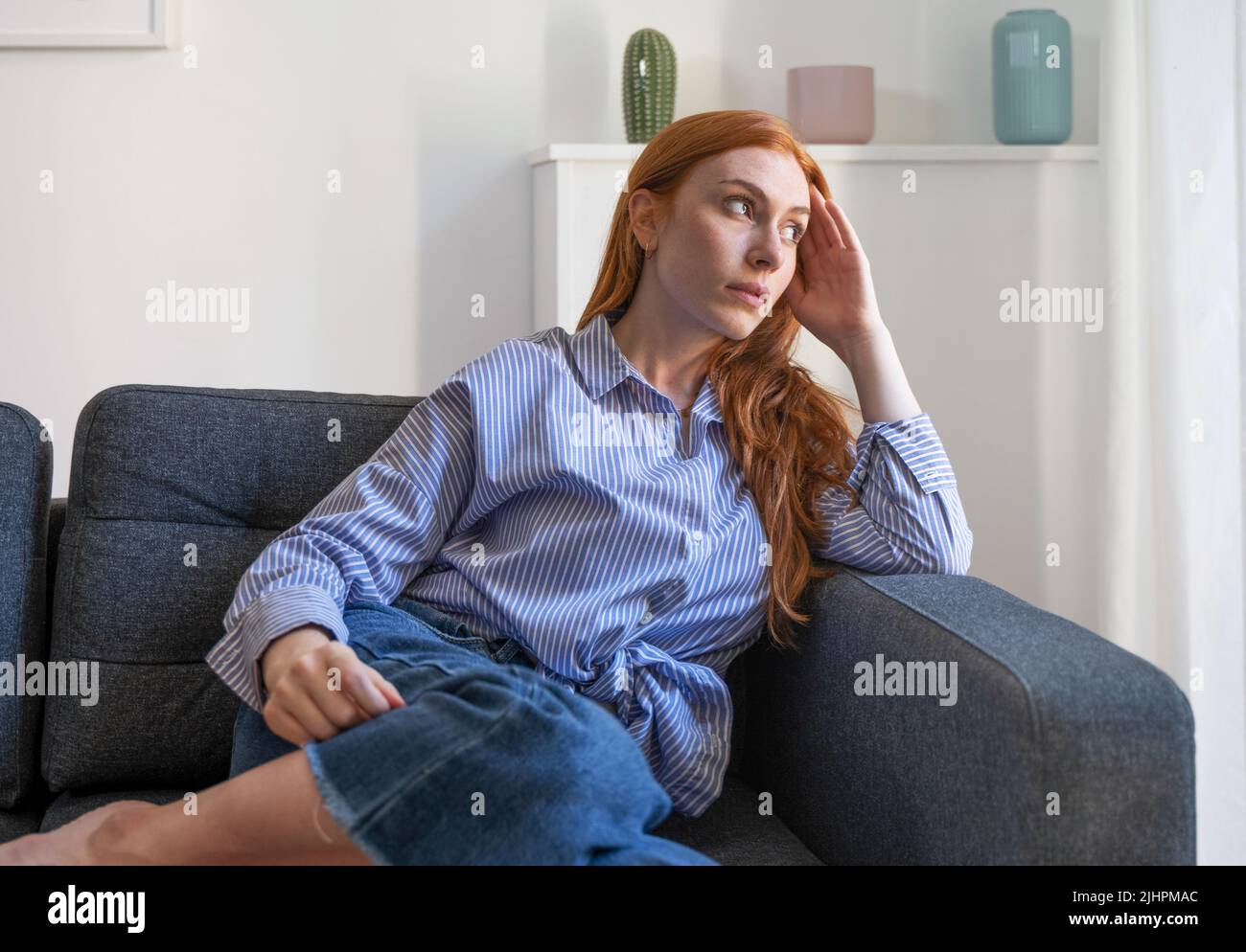 Depressed woman sitting on sofa at home, thinking about life things Stock Photo