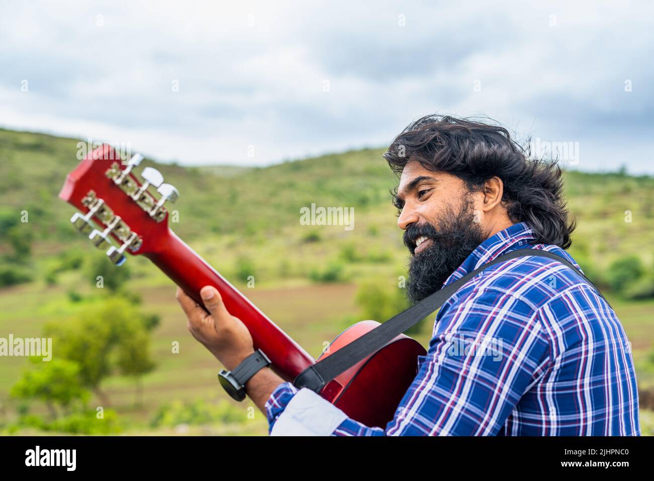 back view shot of musician playing guitar by singing song while sitting on top of hill - concept of hobbies, mindfulness and recreation. Stock Photo