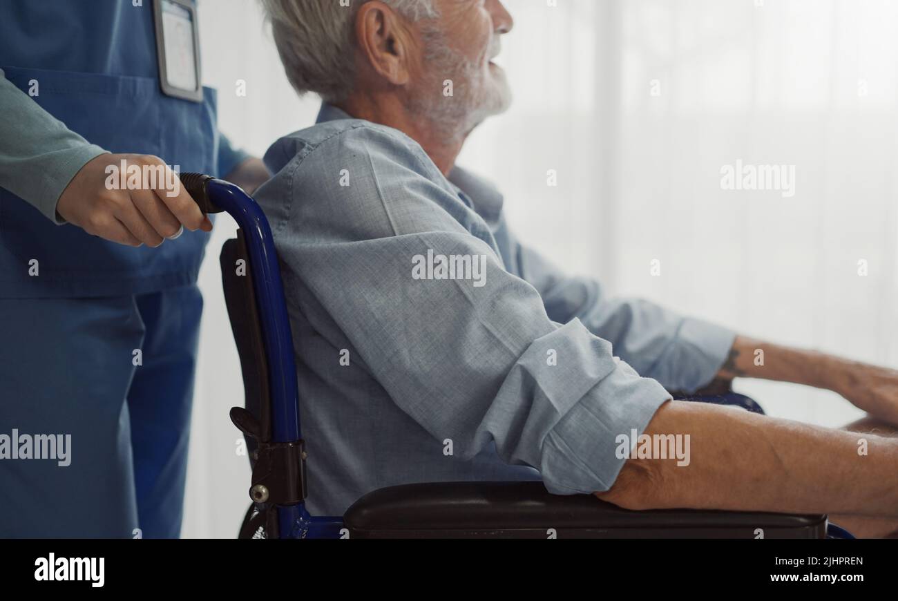 Nurse putting wheelchair with senior man  window. Unhappy senior man having geriatric or depression disease. Therapist taking care, giving support and Stock Photo