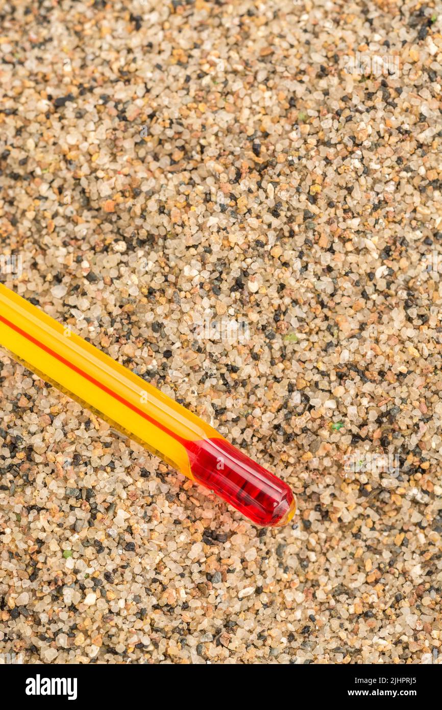 Glass red ink thermometer bulb on coarse sand background. For 2022 Summer heatwave, UK heatwave, hot weather, high temperatures, red hot, severe heat. Stock Photo