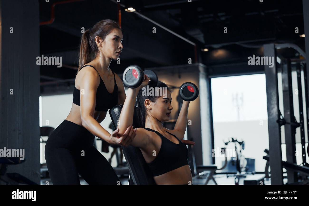 Sporty girl doing weight exercises with the help of her personal trainer at the gym. Stock Photo