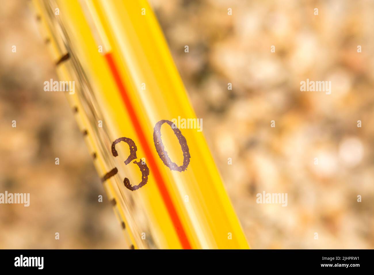 Close-up glass alcohol thermometer on coarse sand, reading 35 C. For 2022 Summer heatwave, UK heatwave, hot weather, high temperatures, severe heat Stock Photo