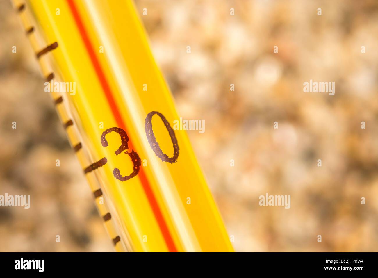 Close-up glass alcohol thermometer on coarse sand, reading 30+ C. For 2022 Summer heatwave, UK heatwave, hot weather, high temperatures, severe heat Stock Photo