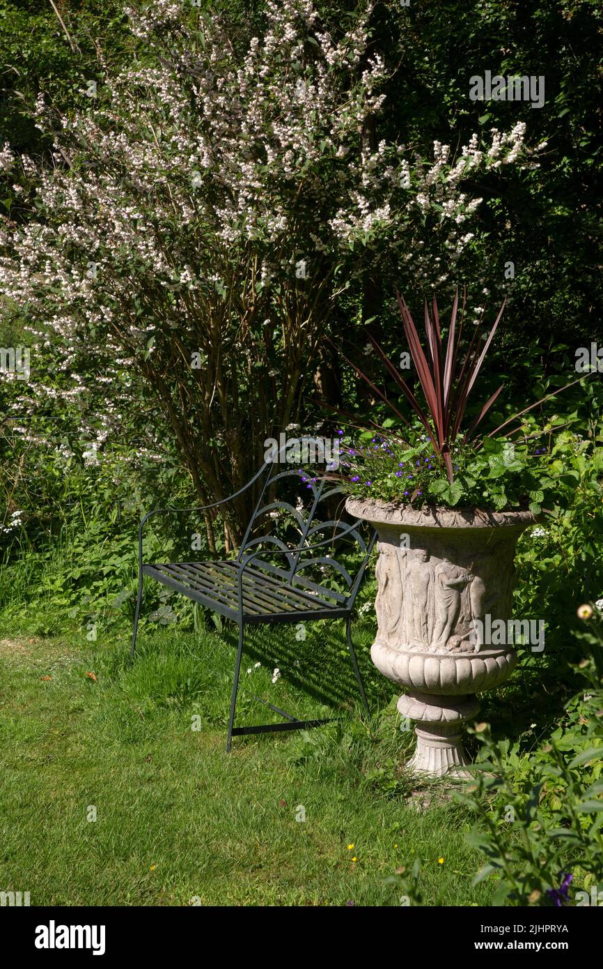 Metal garden bench and feature urn in english summer garden Stock Photo