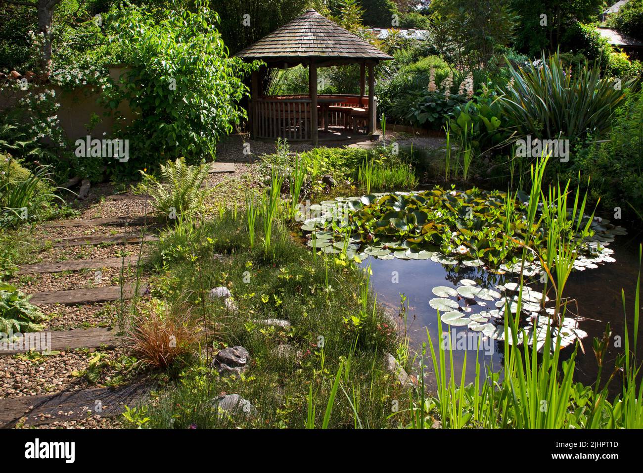 English garden with ornamental pond with summerhouse feature and gravel path with wooden sleepers, England Stock Photo