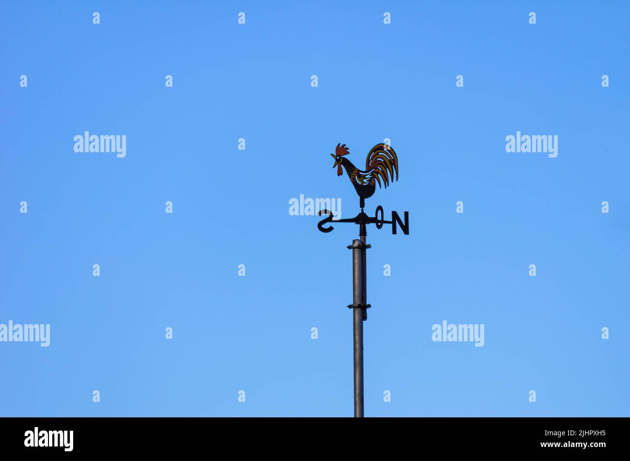 Weather vane or weathercock with wind direction indicator in the form of a compass rose on a roof against a blue sky. Stock Photo