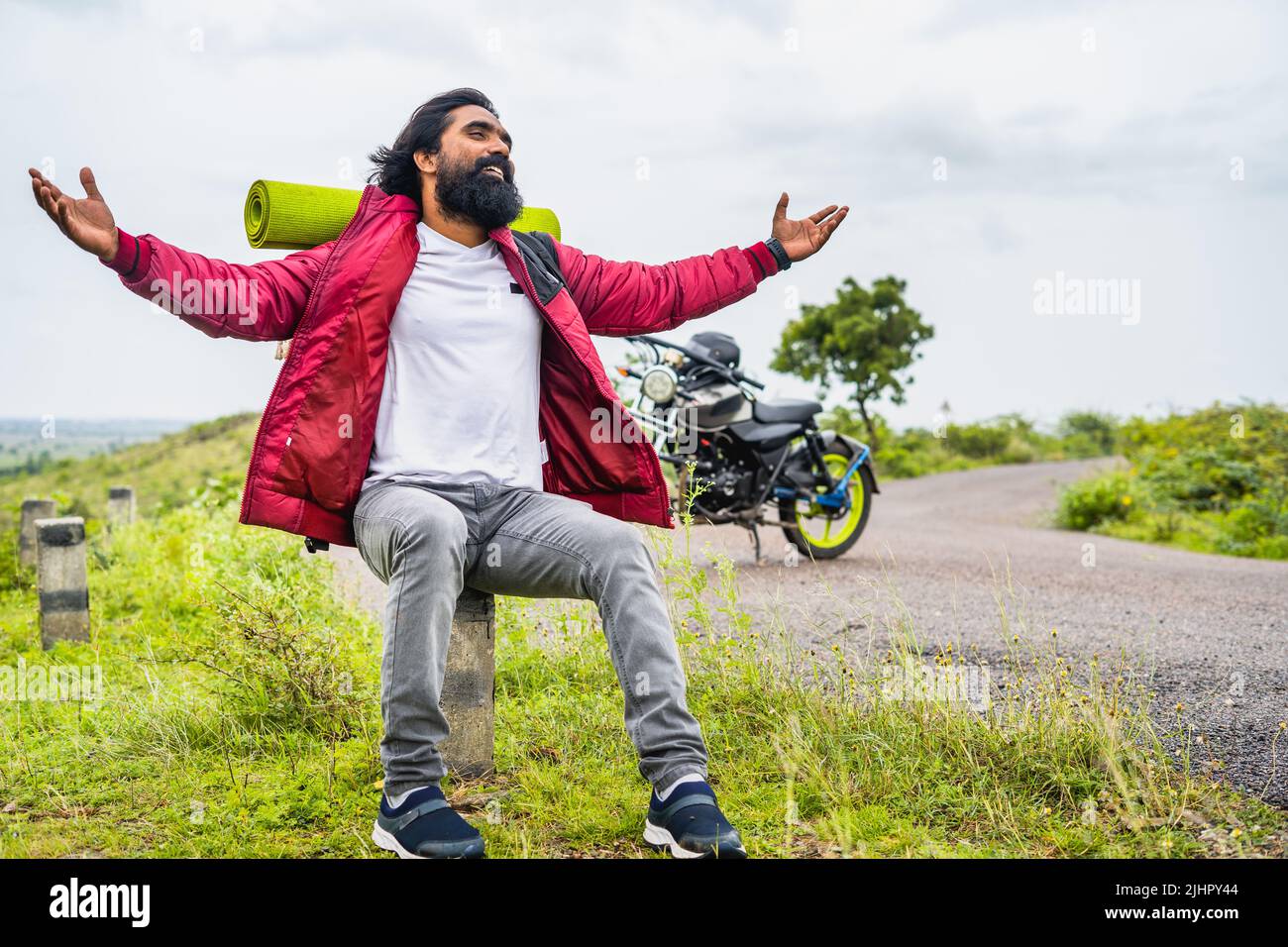 Happy rider feeling nature by stretching arms while sitting on road near highway - concept of weekend holidays, freedom and traveller Stock Photo