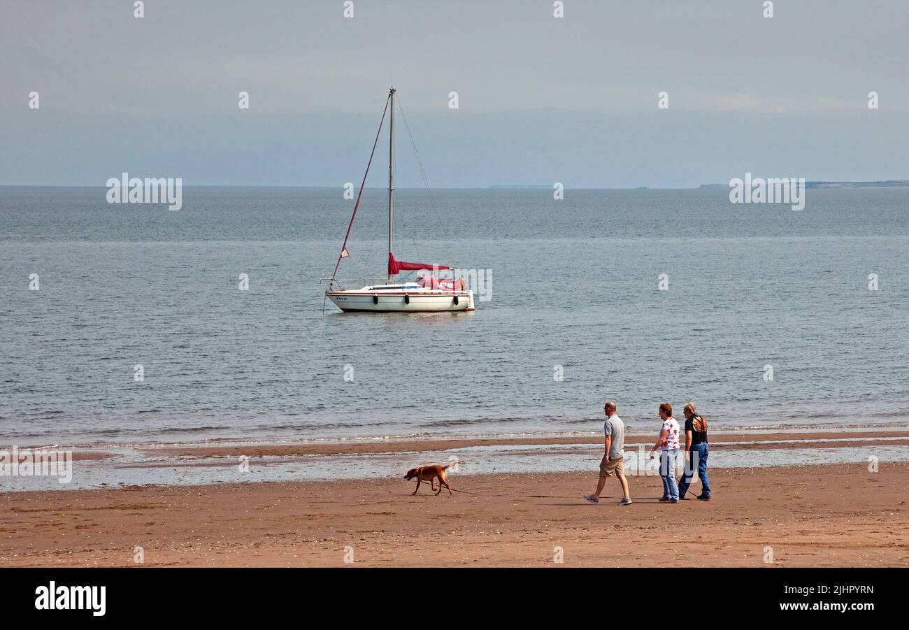 Portobello seaside, Edinburgh, Scotland, UK. 20th July 2022.  Hazy sunshine just around noon with temperature of 22 degrees centigrade for those visiting the shores of the Firth of Forth. Three adults walk along the shore while walking their dog. Credit: Scottishcreative/alamy live news. Stock Photo