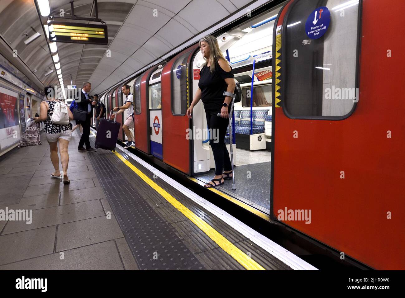 London, England, UK. London Underground - woman with an elbow crutch getting off a tube train Stock Photo