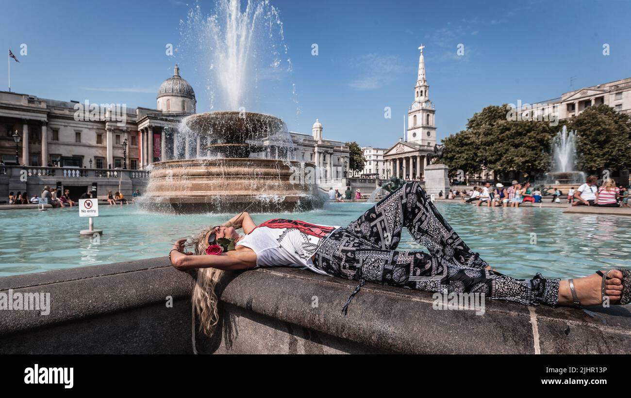 A tourist sunbathes by the Trafalgar Square fountain during the heatwave in London. Stock Photo