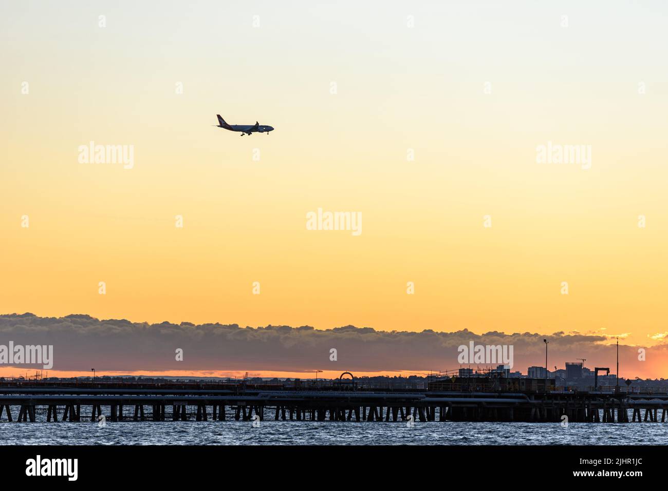 A Qantas plane on its approach to Sydney Airport above Botany Bay at sunset Stock Photo