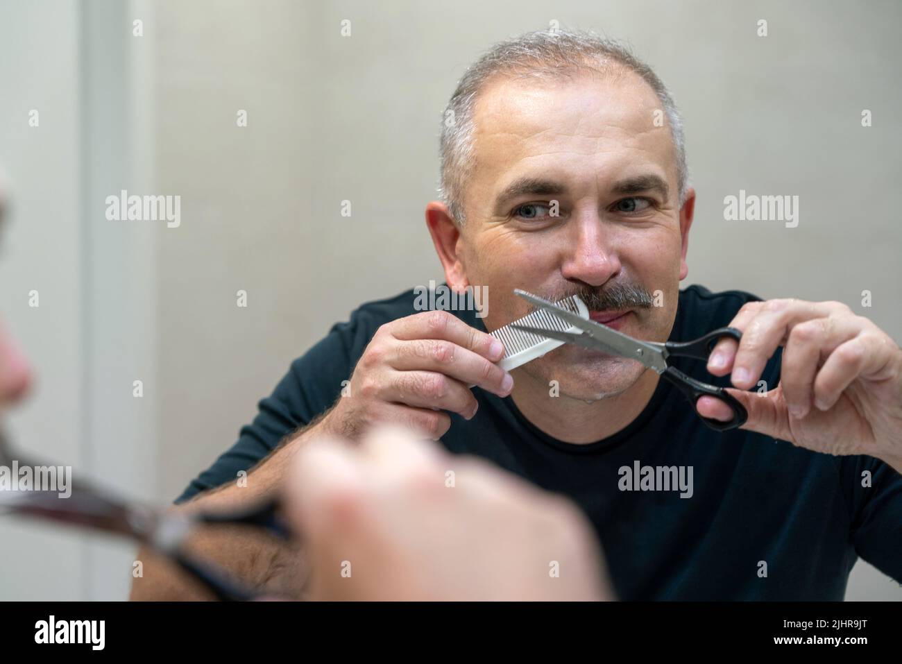 Middle-aged handsome man using scissors to cut his mustache Stock Photo