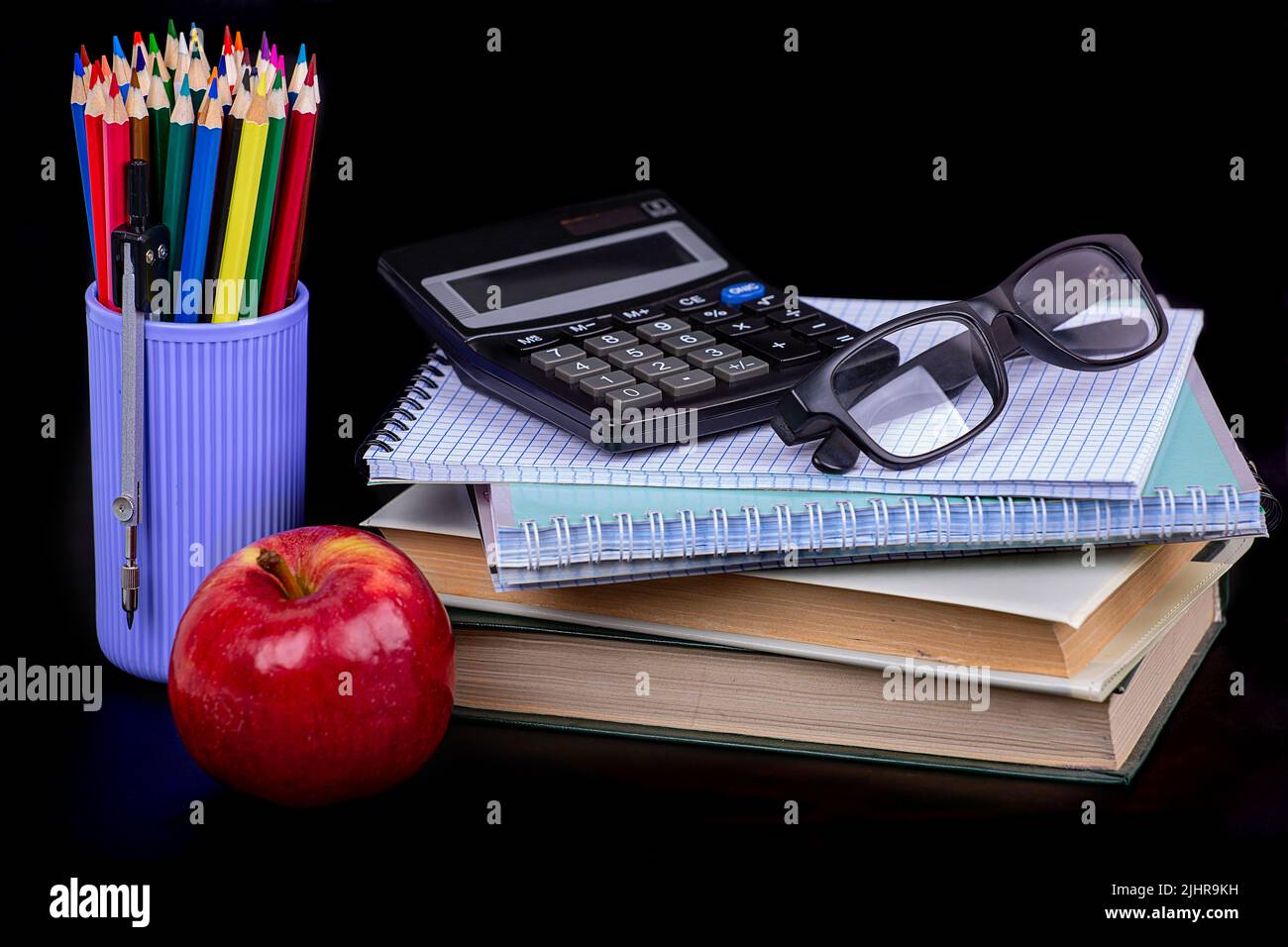 I'm going to school soon. Books, notebooks, calculator, apple, glasses and colored pencils on a black background Stock Photo