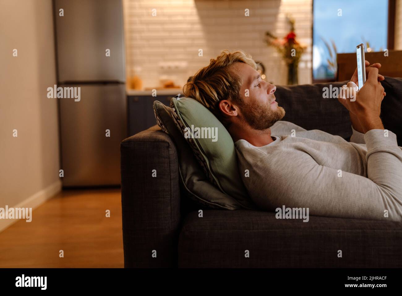 Ginger bristle man using mobile phone while lying on sofa at home Stock Photo