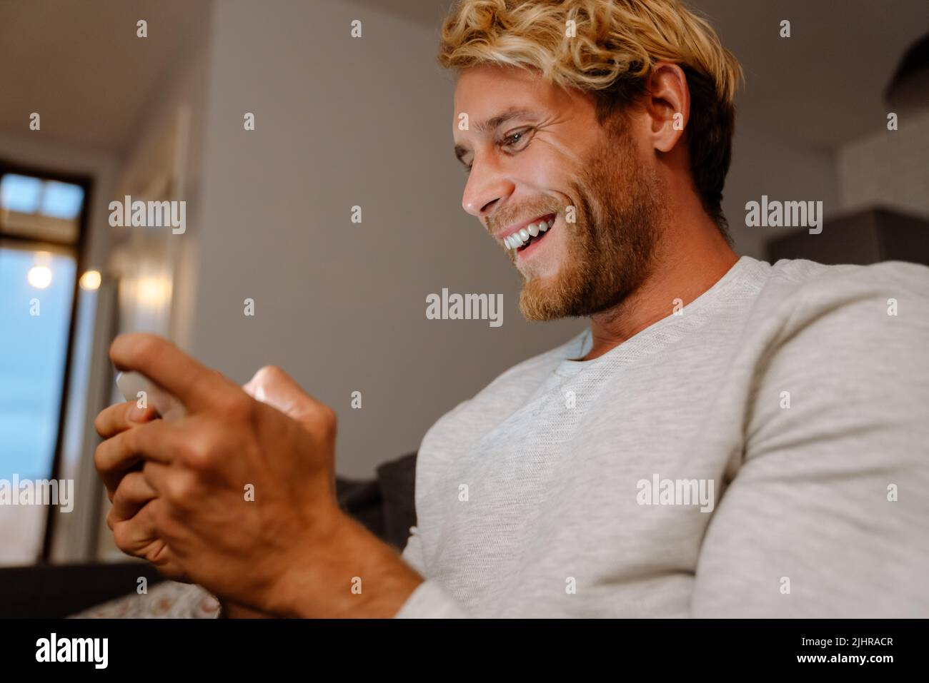 Ginger bristle man using mobile phone while sitting on sofa at home Stock Photo