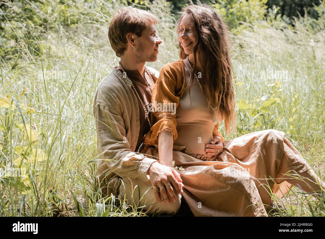 Smiling man hugging pregnant wife on grassy field Stock Photo - Alamy