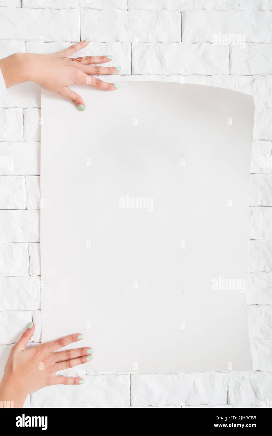 Female hands hanging blank poster to wall mockup Stock Photo