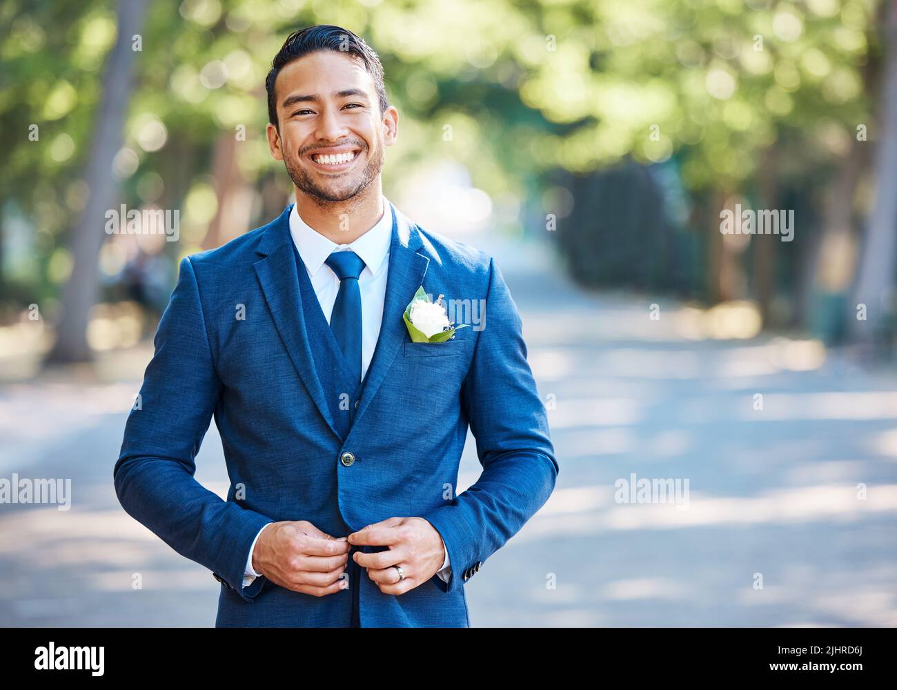 Handsome groom wearing a blue suit with a white shirt and tie. Bridegroom fastening his jacket while standing outdoors on a sunny day Stock Photo