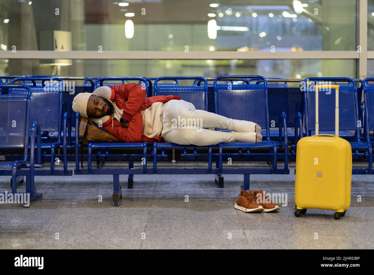 Black guy lying on chairs in airport lounge, can not sleep on an