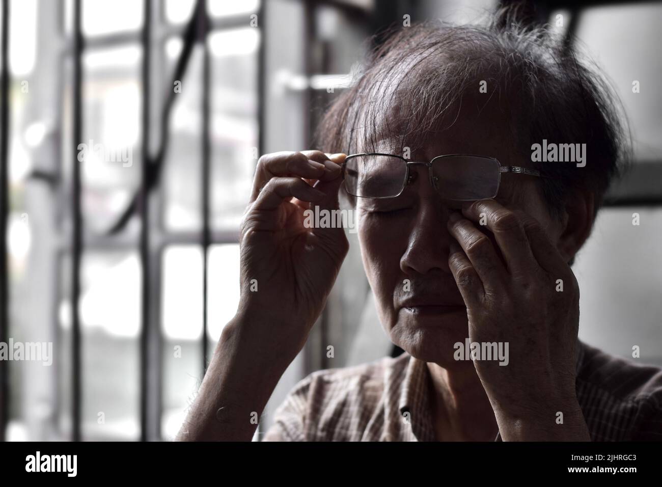 Partial silhouette image of Asian elder man rubbing his eye. Concept of eye pain, strain or itchy eyelid. Stock Photo