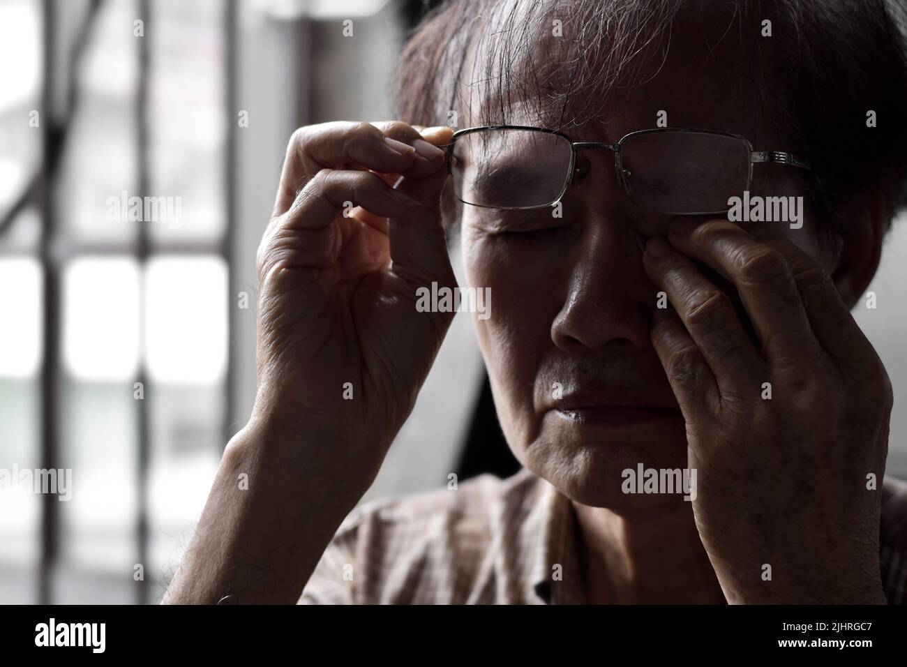 Partial silhouette image of Asian elder man rubbing his eye. Concept of eye pain, strain or itchy eyelid. Stock Photo