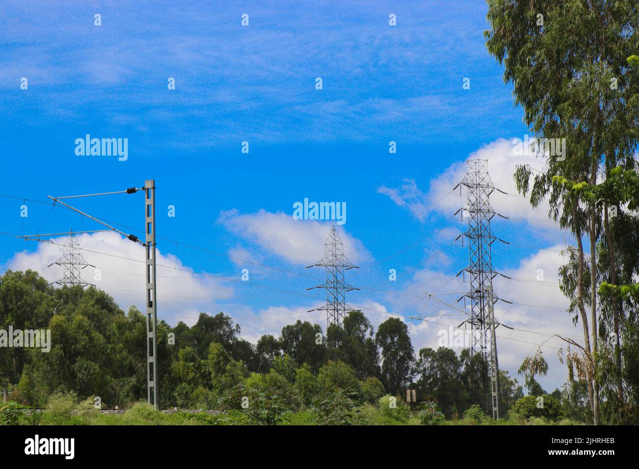 Electricity pole or electric post running through forests along with a view of electric train catenary against sky background Stock Photo
