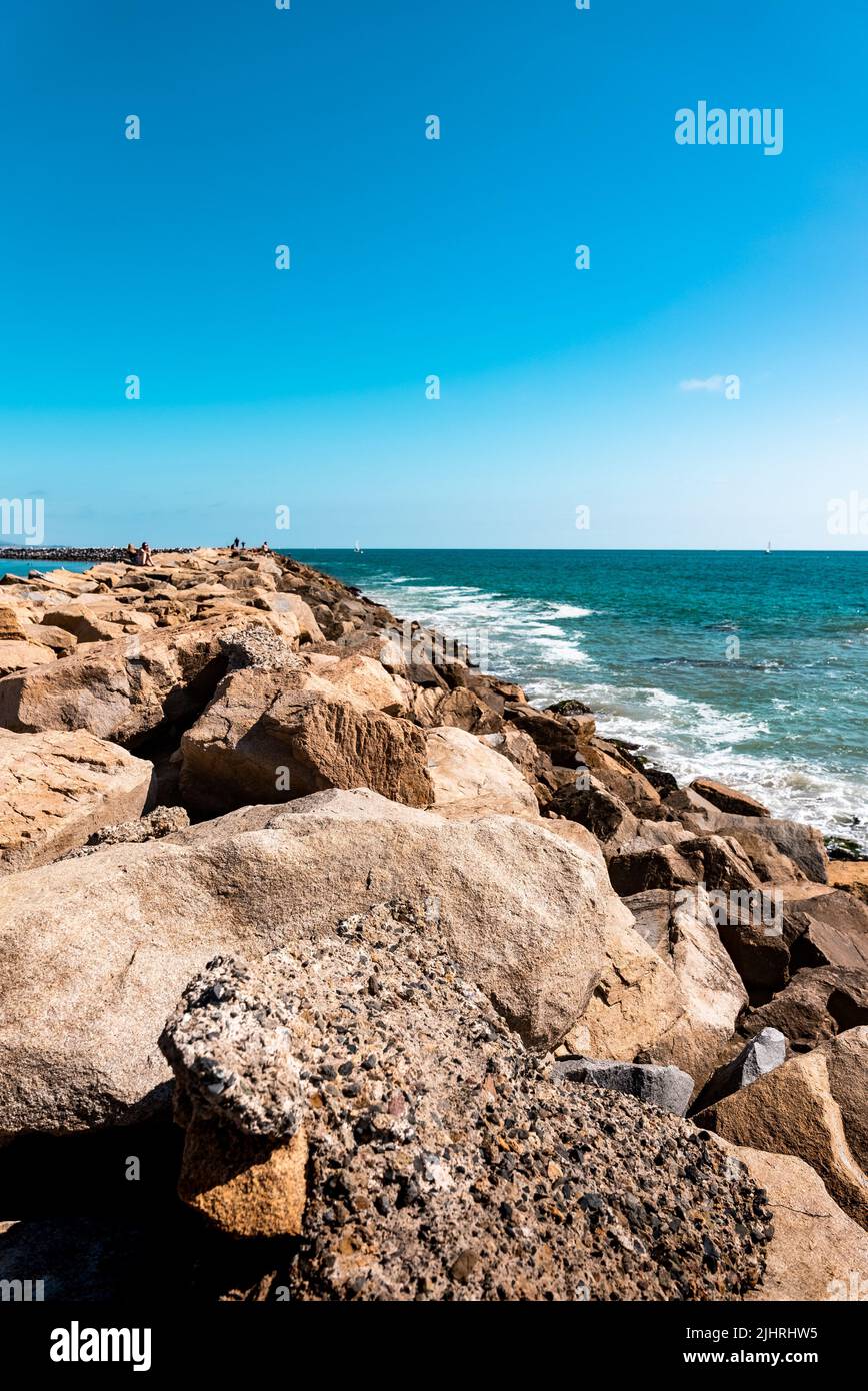 A vertical shot of a rocky shore on the Dana Point under a blue sky ...