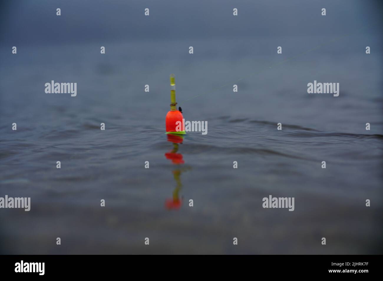 https://c8.alamy.com/comp/2JHRK7F/an-orange-and-green-fishing-bobber-floating-in-the-water-2JHRK7F.jpg
