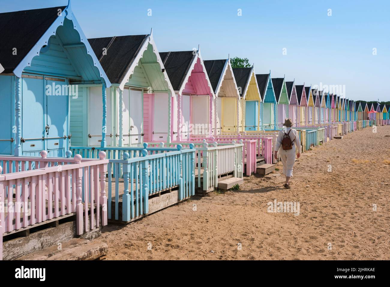 Woman female holiday vacation alone, view in summer of a solo female traveler walking past colorful beach huts on a sandy beach, England, UK Stock Photo