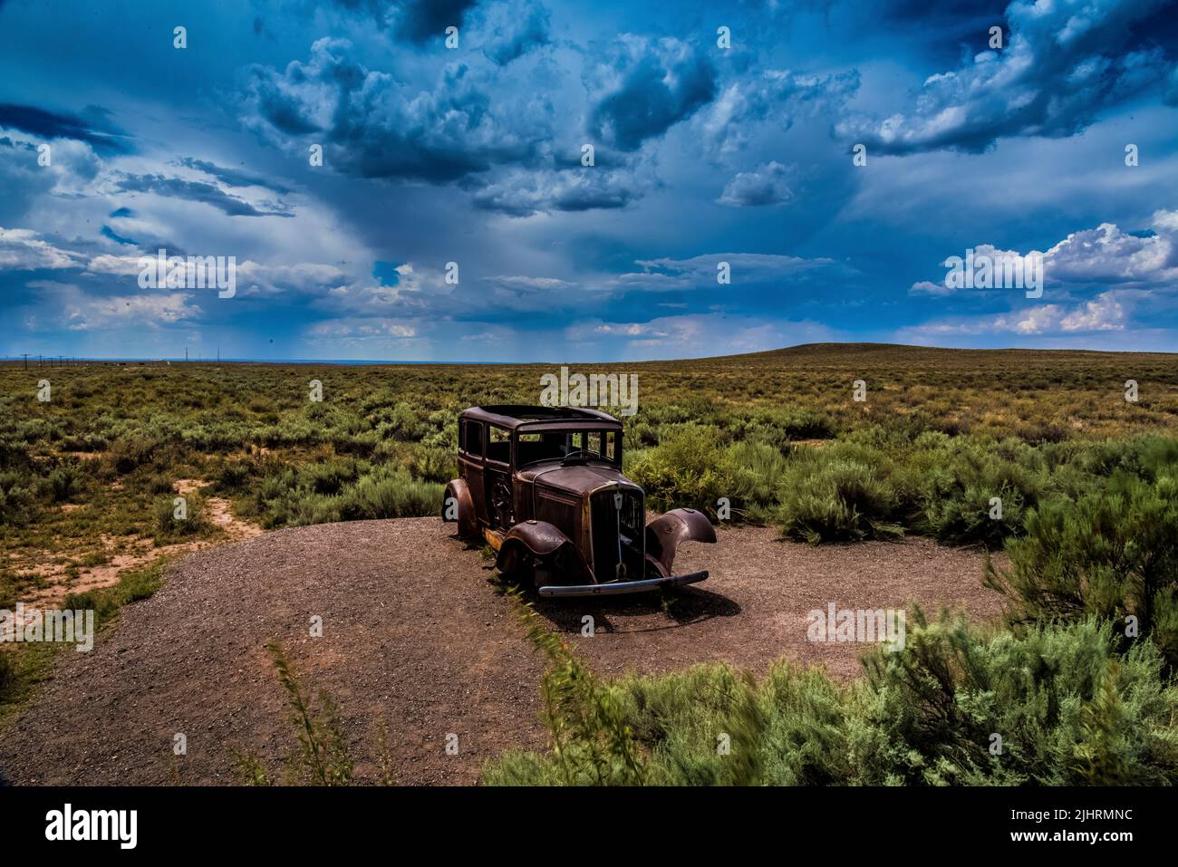 A rusty old abandoned vintage car in a greenfield under a blue sky ...