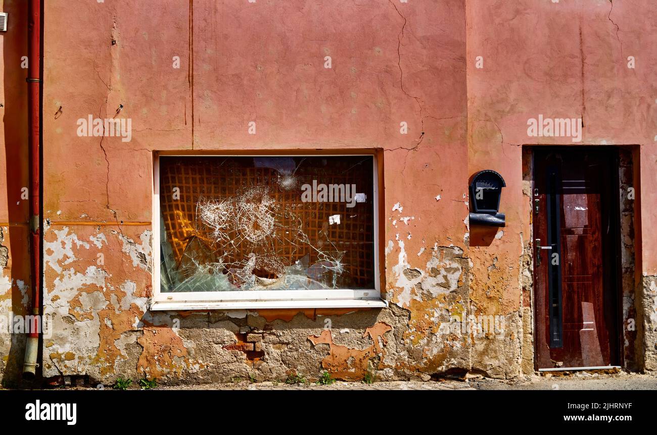 Peeling paint on a dilapidated facade with a rain gutter, a wooden door and a shop window whose