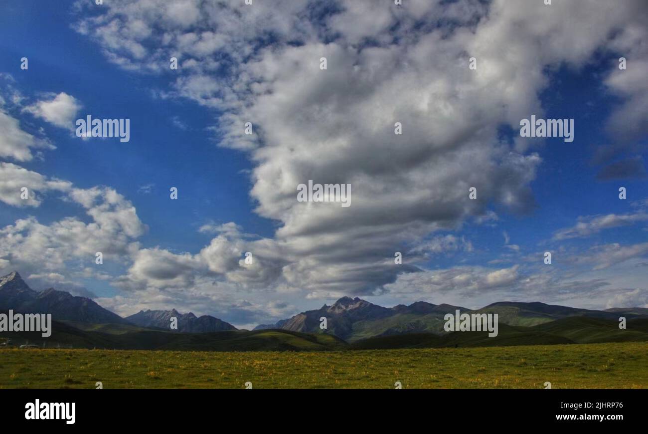 A landscape with large meadows with dark mountains under cloudy blue ...