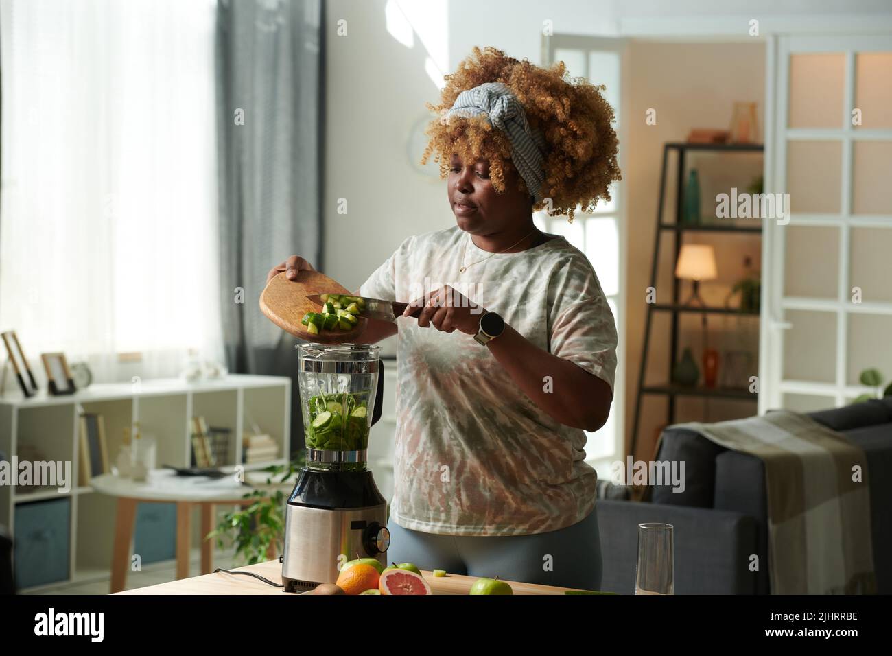 African girl with curly hair adding cutted pieces of cucumber in ...