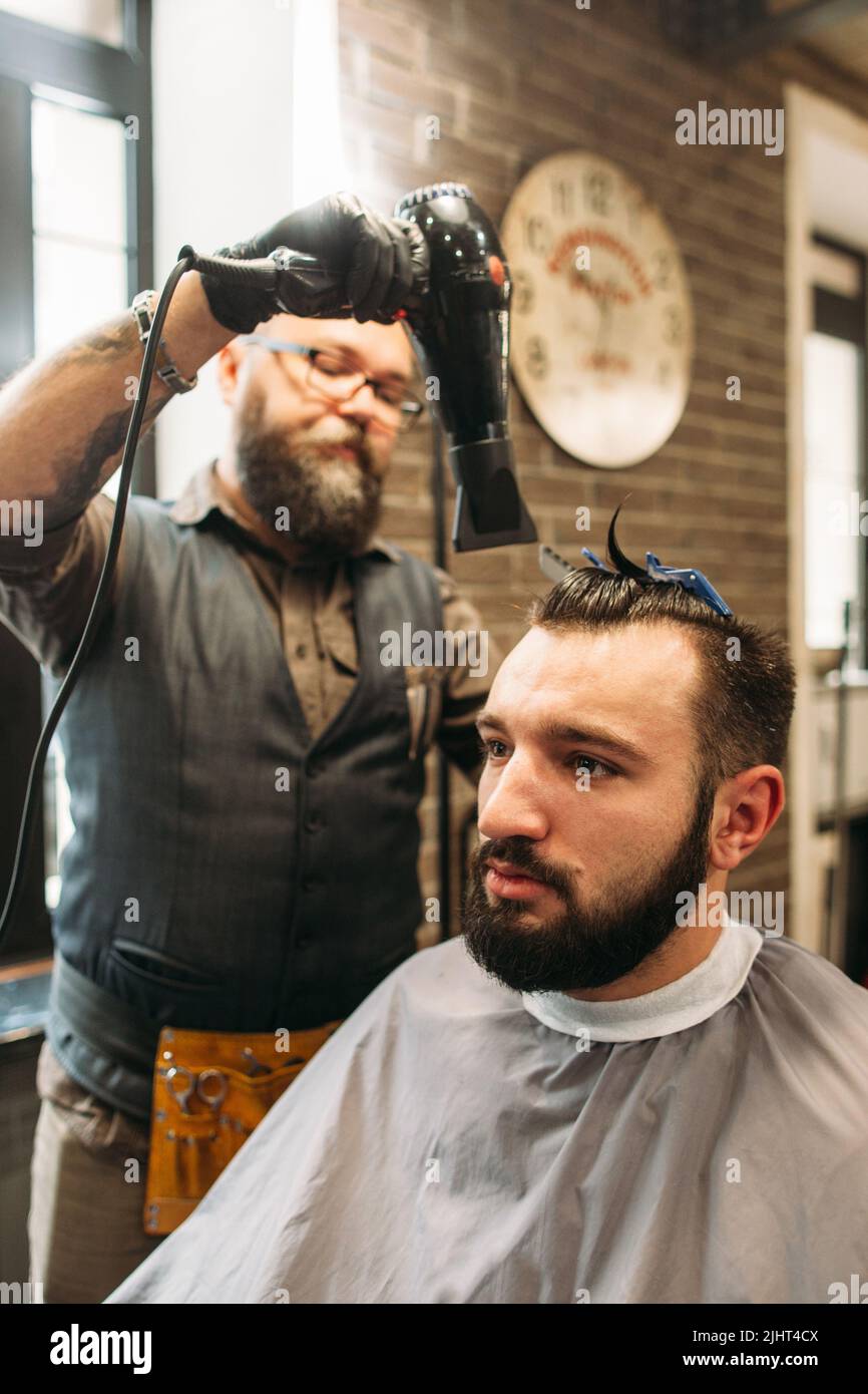 Stylish barber drying mans hair in barbershop Stock Photo
