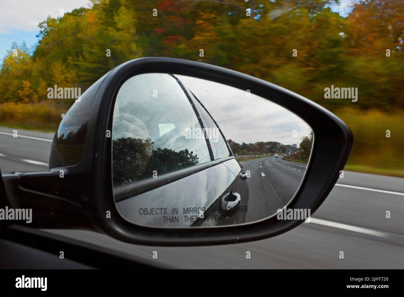 Car Side View Mirror on Passenger Door with view of Highway and Fall Foliage Stock Photo