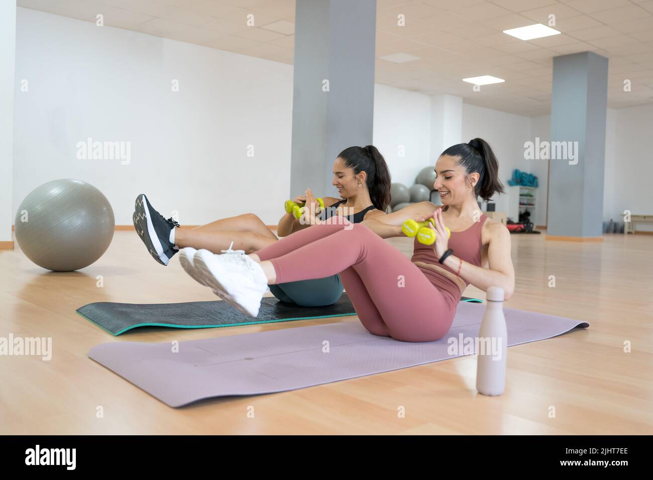 TWO GIRLS TRAINING YOGA AND PILATES TOGETHER WITH A BALL AND WEIGHTS