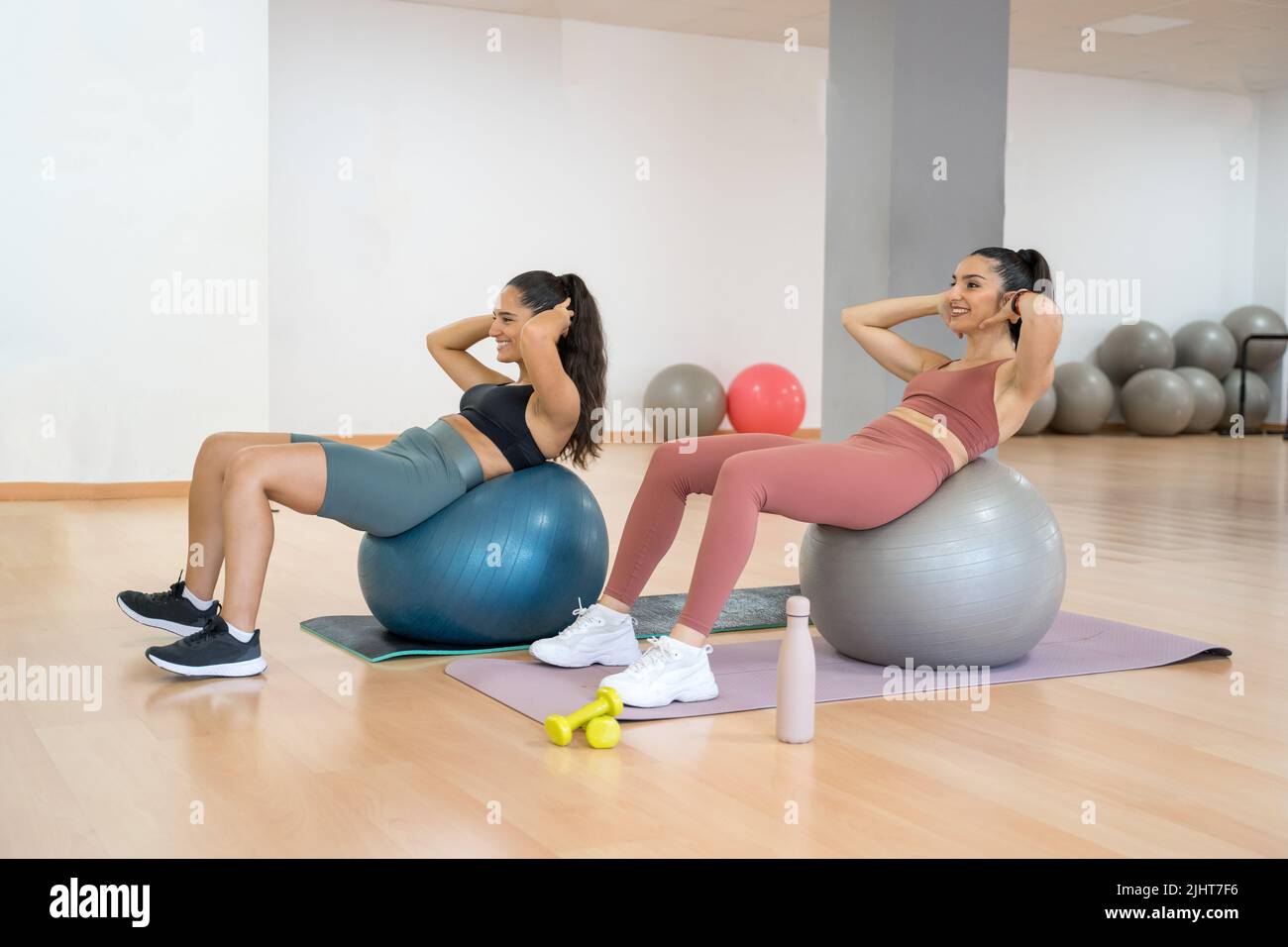 TWO GIRLS TRAINING YOGA AND PILATES TOGETHER WITH A BALL AND WEIGHTS