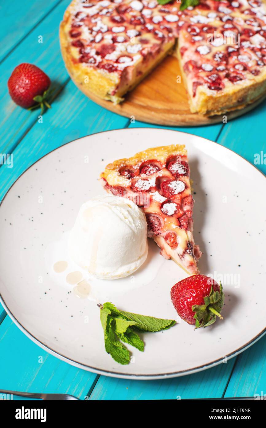 Homemade strawberry custard tart decorated with strawberry and ice cream on blue wooden background. Stock Photo