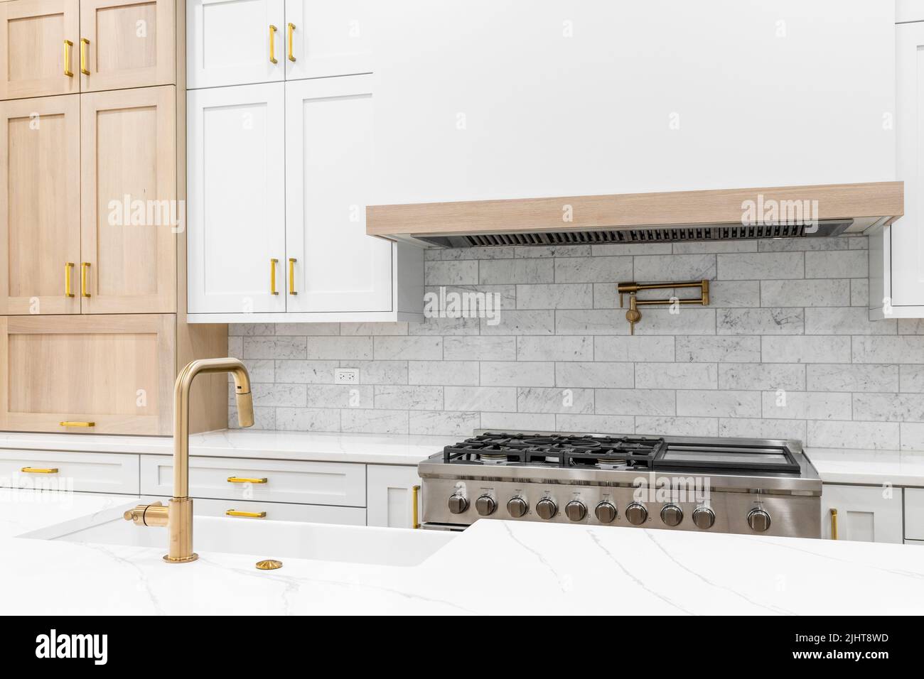 A kitchen detail shot with a gold faucet, white and wood cabinets, marble countertop, and subway tile backsplash. Stock Photo