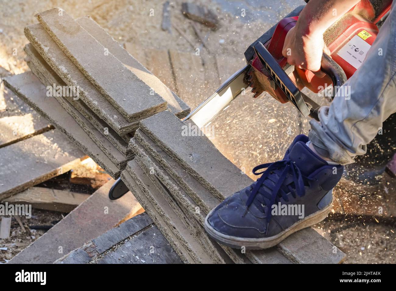 Cutting old wooden chipboards with electric chainsaw, splinters flying