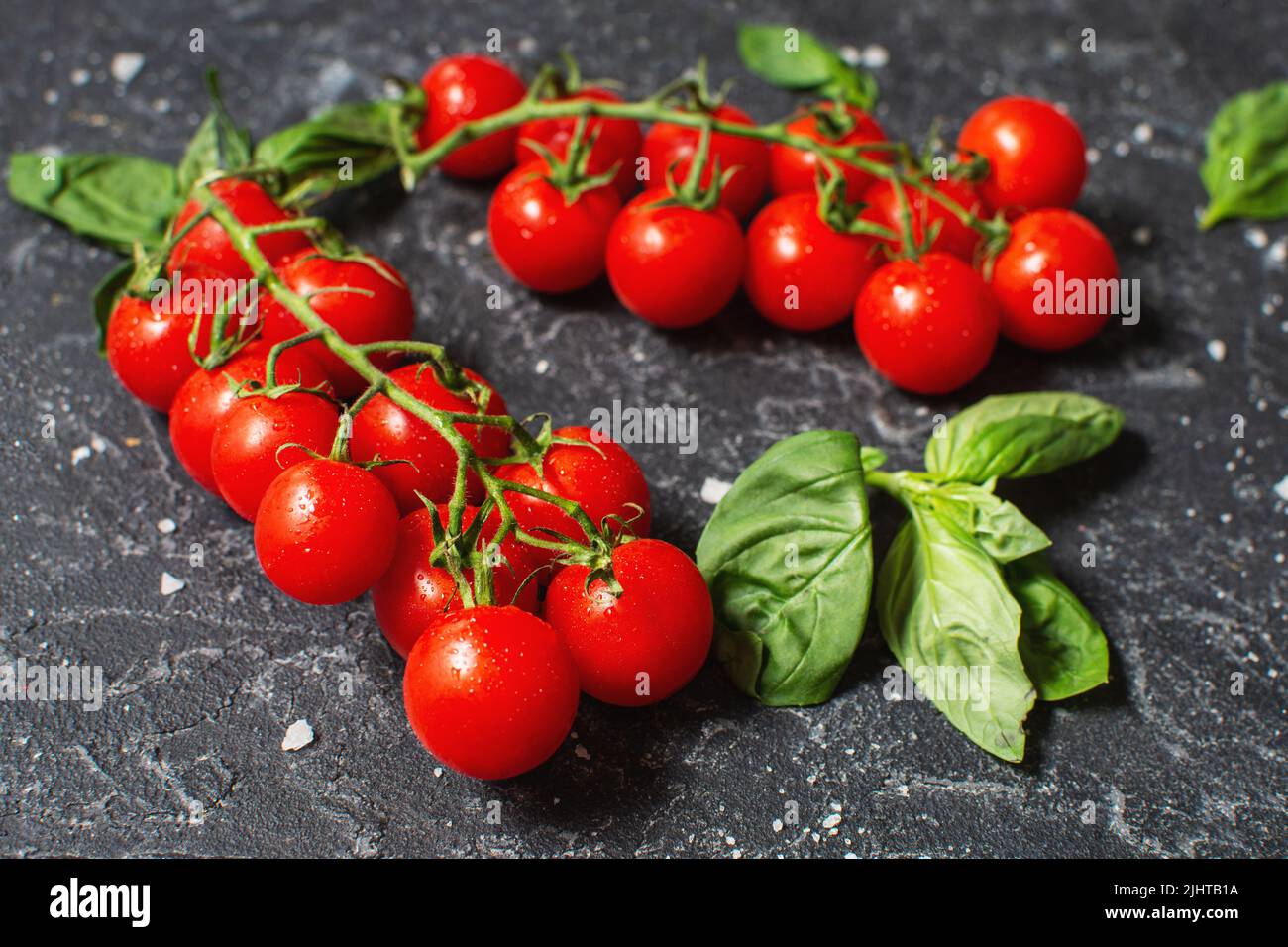 Fresh cherry tomatoes and basil with spices on a black stone background. Stock Photo
